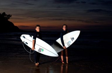 Chico y chica en la orilla con tablas de surf al anochecer